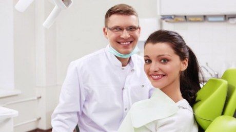 Zahnarzt und Patientin blicken freundlich lächelnd in die Kamera
