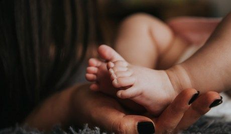 Eine Frauenhand hält die Füße eines Säuglings